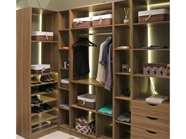 Closet embutido marrom de canto com diversas prateleiras com roupas, calçados e cestos, com fita de LED interna.