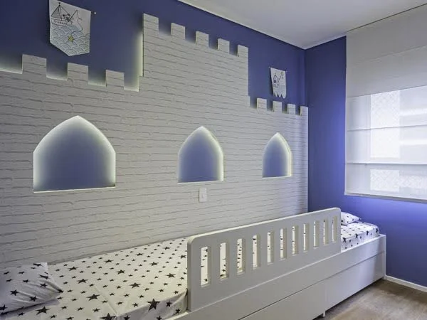 Quarto azul com cama branca e desenho de castelo na parede com fita de LED no seu contorno.