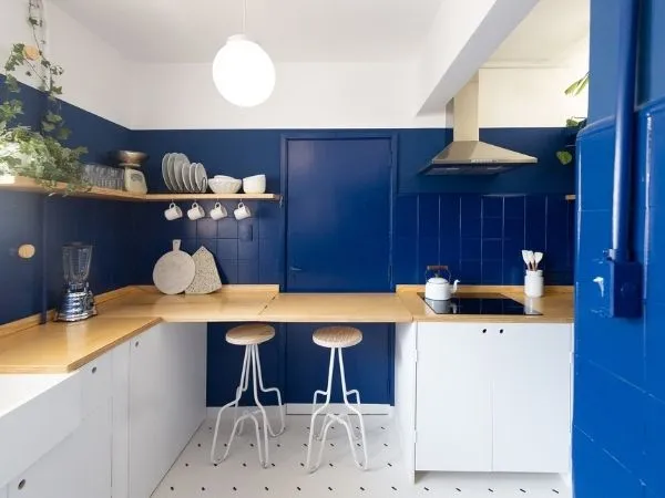 Bancada amadeirada de uma cozinha pequena com objetos decorativos, como prateleiras, xícaras, plantas e lâmpadas brancas.
