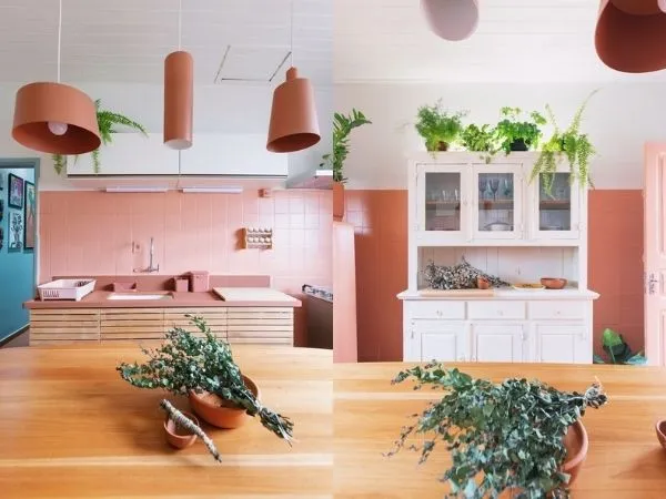 Cozinha com azulejo pintado de rosa, mesa de madeira e armário branco.