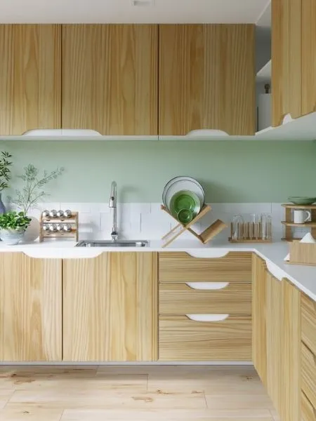 Cozinha com parede verde-clara e armários de parede e de chão em tom de madeira clara.