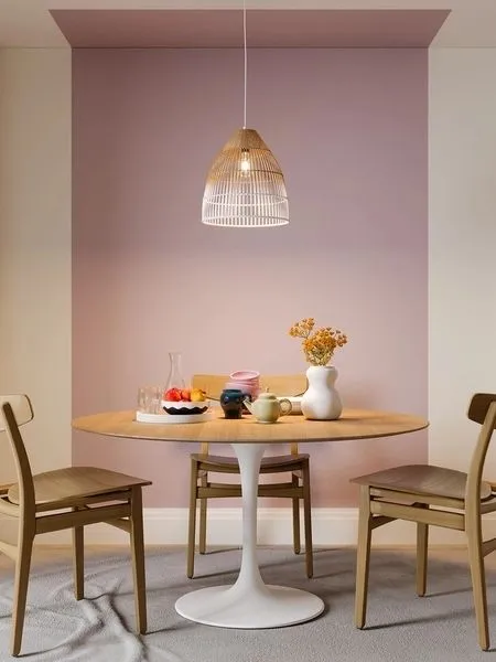Cômodo branco com mesa redonda e cadeiras de madeira, com pintura setorizada em faixa do chão ao teto rosa.
