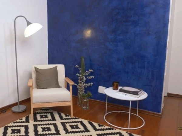 Cômodo com parede marmorizada azul, poltrona e mesa de apoio brancas.