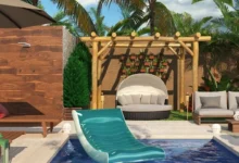 Área externa com piscina com bóia, espreguiçadeiras e bancos em volta, assim como um pergolado e árvores.