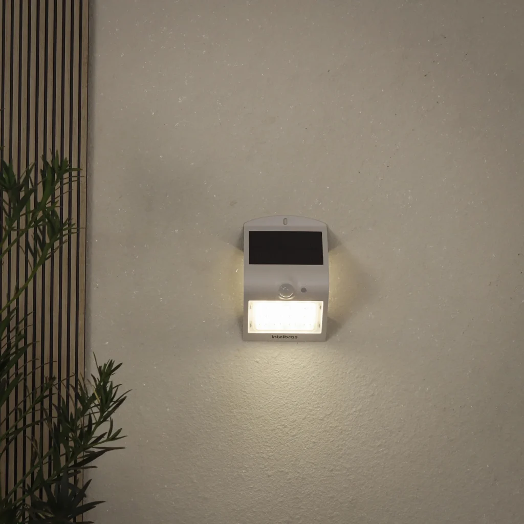 Parede externa de cor clara sendo iluminada por uma arandela solar branca.