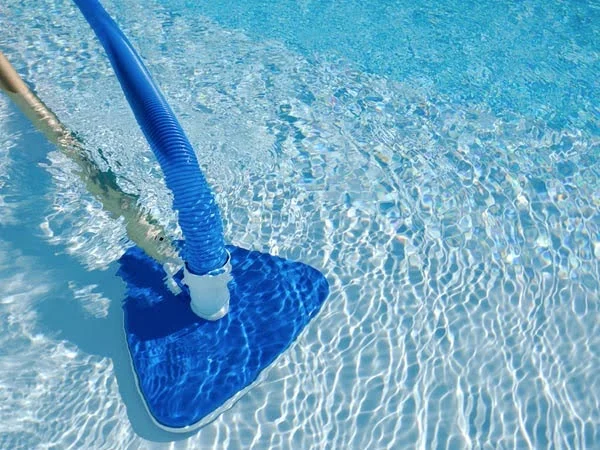 Piscina tendo seu fundo aspirado por um aspirador de piscina azul com acabamento retangular.