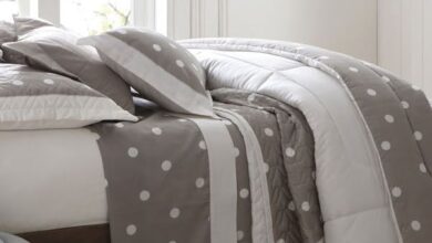 Imagem de uma cama queen coberta por um edredom de cor clara.