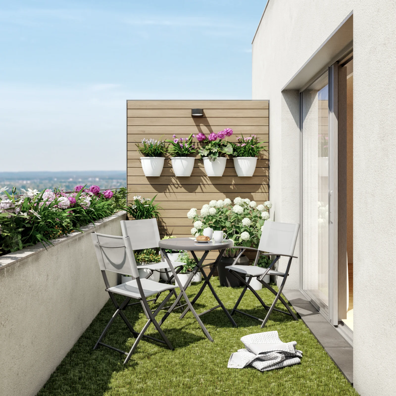 Área externa com 3 cadeiras e uma mesa de tons claros, além de vasos e flores pendurados.