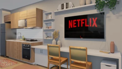 Projeto de studio com parede clara, mesa encostada na parede com duas paredes, uma televisão acima dela e nichos brancos e prateleira ao seu redor.