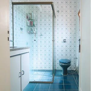 Banheiro com piso e privada azuis, azulejos brancos com detalhes azuis e gabinete branco.