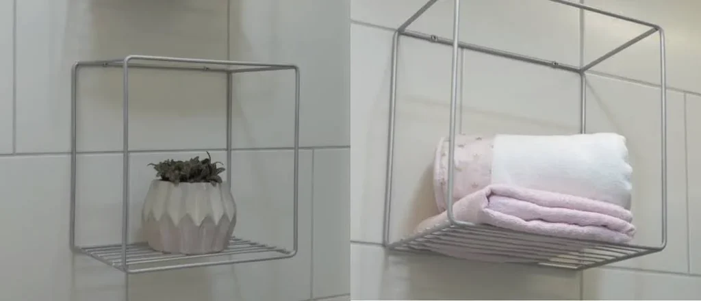 Ao lado esquerdo, um nicho de metal com um vaso de plantas, ao lado direito, o mesmo nicho com toalhas.